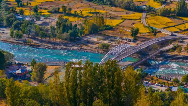 A beautiful aerial view of a bridge over a river surrounded by vibrant autumn fields in Ganderbal.
