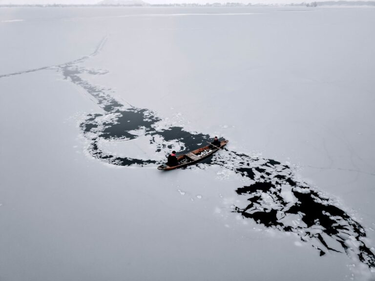 Men navigating a boat through icy waters on a frozen lake in Srinagar.