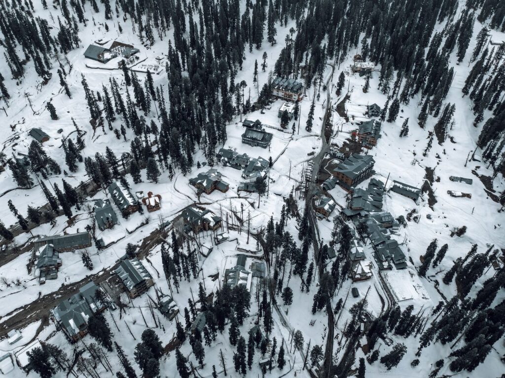 Snow-covered aerial view of Gulmarg, showcasing buildings and pine trees in winter.