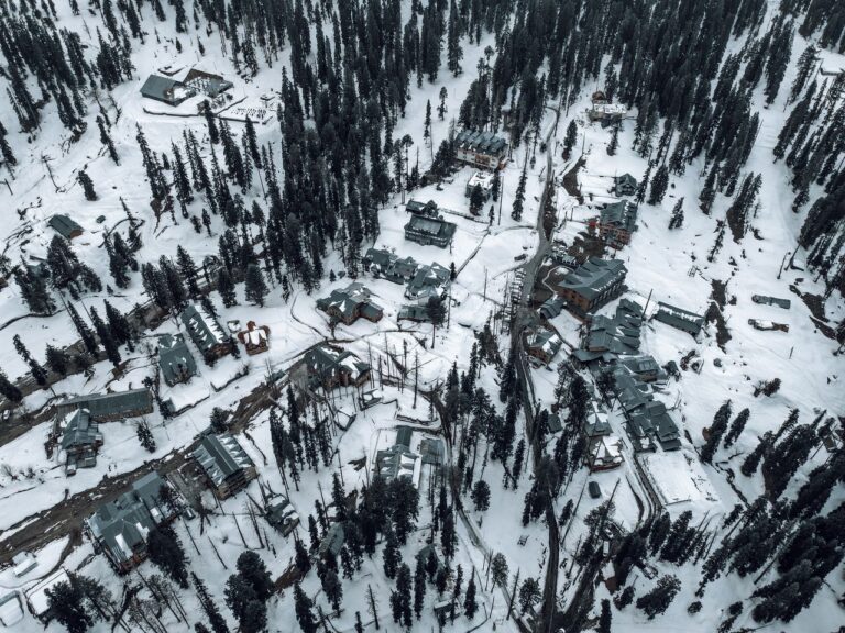Snow-covered aerial view of Gulmarg, showcasing buildings and pine trees in winter.